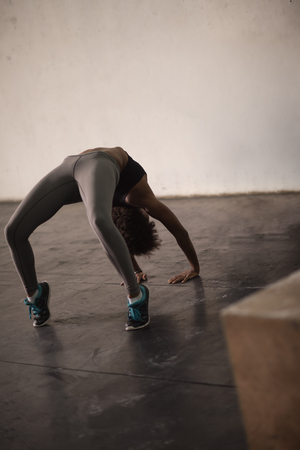 Beautiful young african american woman working out , doing yoga exercise, stretching, standing in Bridge Pose in the gymの写真素材