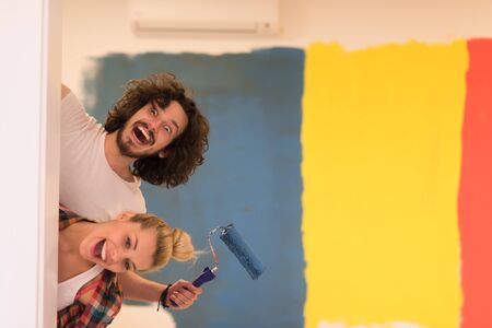 portrait of happy smiling young couple painting interior wall of new house  peeking from behind the wallの写真素材