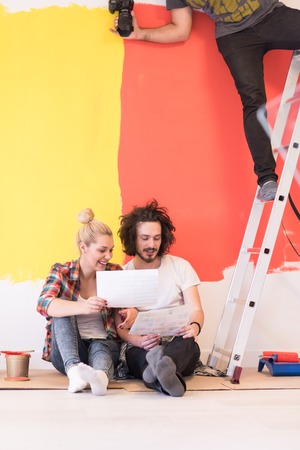 Happy young couple relaxing after painting a room in their new house on the floorの写真素材