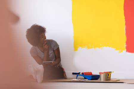 Portrait of a beautiful african american female painter sitting on floor near wall after painting.の写真素材