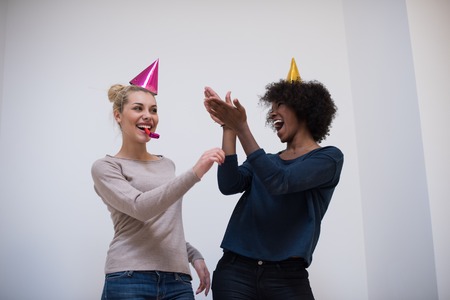 people and celebration concept  young multiethnics smiling women in party caps blowing to whistlesの写真素材