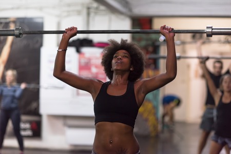 Young Cute african american sport woman in fitness room lifting empty barの写真素材