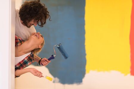 portrait of happy smiling young couple painting interior wall of new house  peeking from behind the wallの写真素材