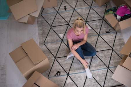 top view of young beautiful woman sitting and relaxing on the floor after moving into a new home with cardboard boxes around herの写真素材