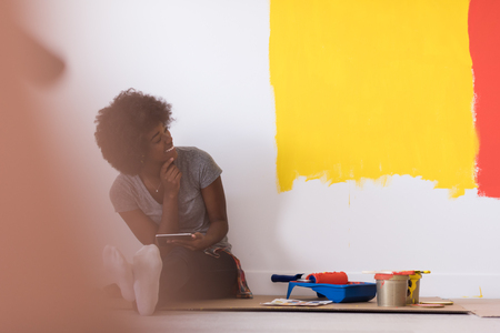 Portrait of a beautiful african american female painter sitting on floor near wall after painting.の写真素材