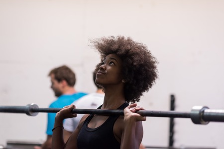 Young Cute african american sport woman in fitness room lifting empty barの写真素材