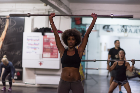 Young Cute african american sport woman in fitness room lifting empty barの写真素材