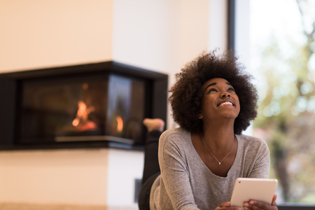 beautiful young black women using tablet computer on the floor of her luxury home in front of fireplace at autumn dayの写真素材