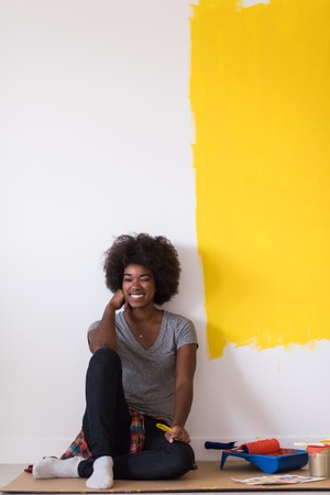 Portrait of a beautiful african american female painter sitting on floor near wall after painting.の写真素材