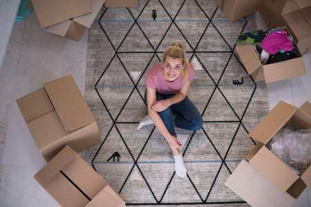 top view of young beautiful woman sitting and relaxing on the floor after moving into a new home with cardboard boxes around herの写真素材