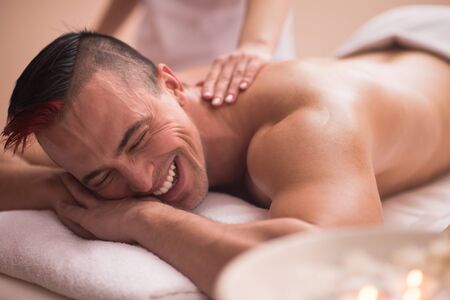 Positive young man having a back massage in a spa centerの写真素材