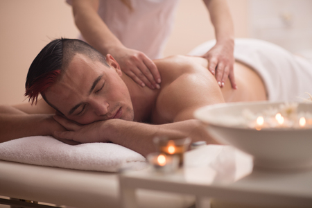 Positive young man having a back massage in a spa centerの写真素材