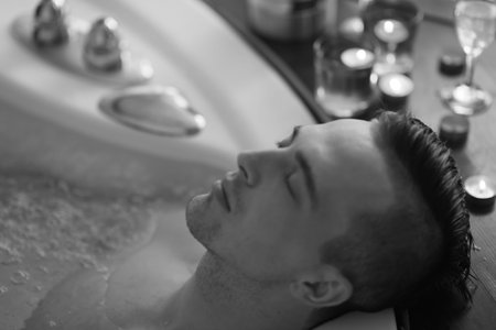 young handsome man enjoys relaxing in the hot tub with candles and champagne at luxury resort spa