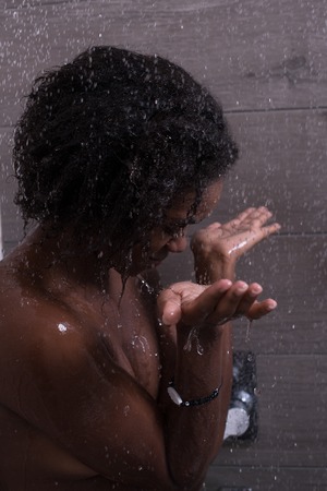 Woman in the shower,beautiful black young female showering under refreshing water, healthy lifestyle, enjoying time in luxury spa resortの写真素材