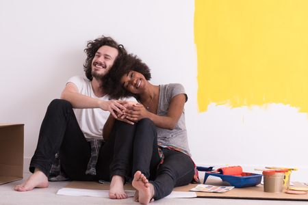 Happy young multiethnic couple relaxing after painting a room in their new house on the floorの写真素材