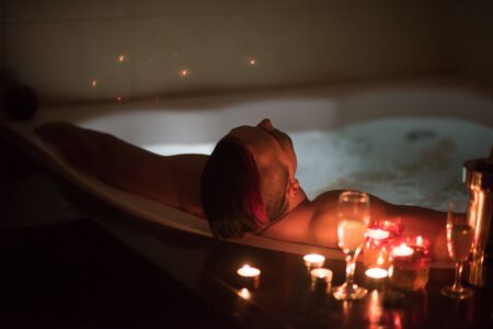 young handsome man enjoys relaxing in the hot tub with candles and champagne at luxury resort spaの写真素材