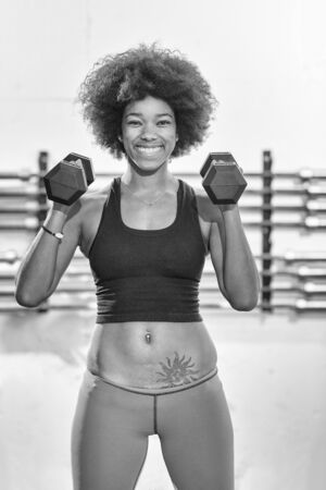 young beautiful African American woman doing bicep curls in a gymの写真素材