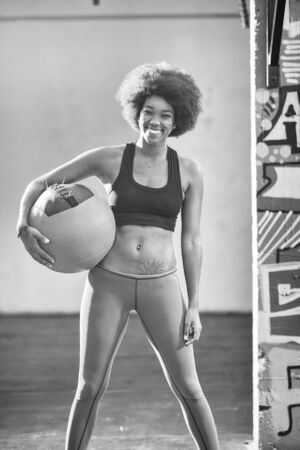 portrait of a young beautiful African American women carrying crossfit ball in gymの写真素材
