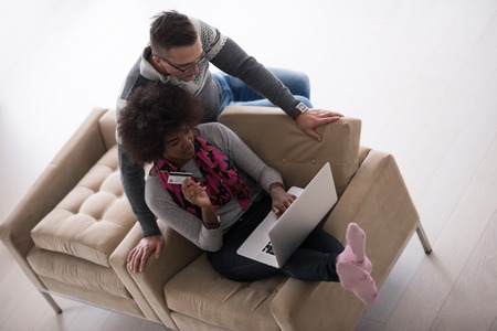 Happy young multiethnic couple shopping online through laptop using credit card at homeの写真素材