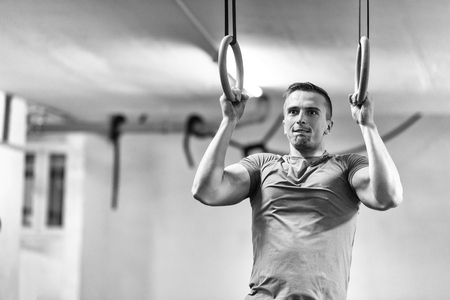 Fitness handsome man doing dipping exercise using rings in the gymの写真素材