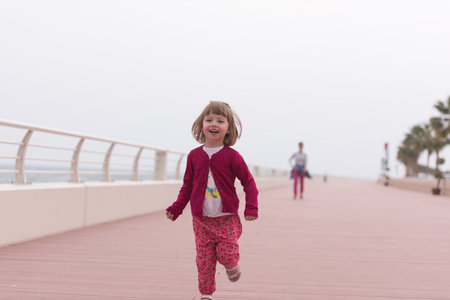 young mother and cute little girl running and cheerfully spend their time on the promenade by the seaの写真素材