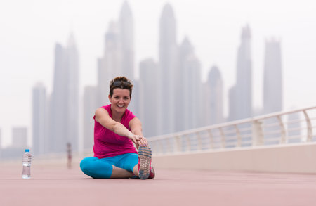 very active young beautiful woman stretching and warming up on the promenade along the ocean side...