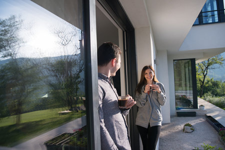 young beautiful handsome couple enjoying morning coffee on the door of their luxury home villaの写真素材
