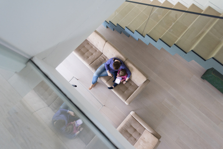 Beautiful young mother and her cute little daughter are using a tablet and smiling, sitting on sofa at home top viewの写真素材
