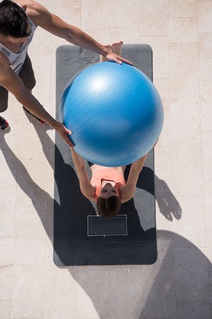 young beautiful woman and personal trainer doing exercise with pilates ball in front of her luxury homeの写真素材