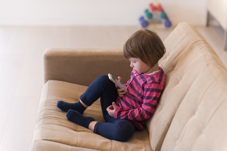 Portrait of cute little girl playing games on smartphone at homeの写真素材