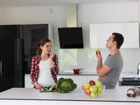Young handsome couple in the kitchen  beautiful woman preparing a salad while the man eating an...