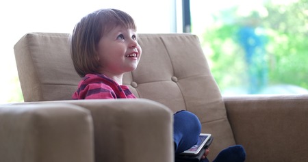 Cute little girl  sitting on coutch and using touchpad or tablet and smilingの写真素材