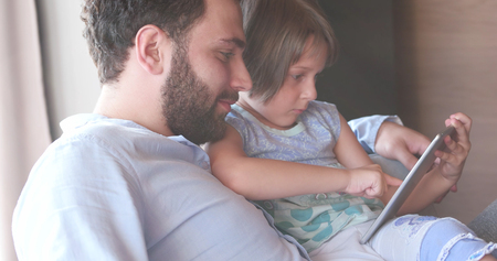 Father Daughter sitting in sofa  playing games on tabletの写真素材