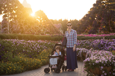 young mother and cute little girl in a baby stroller enjoying a beautiful day in the flower gardenの写真素材
