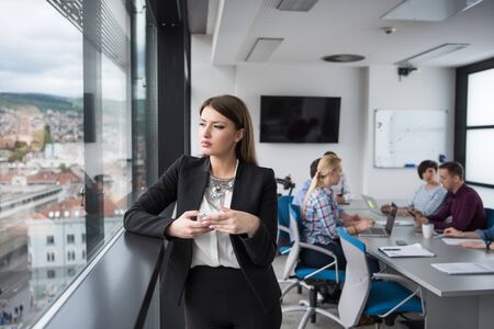 businesswoman speeking on phone beside window of modern officeの写真素材