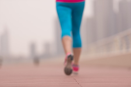 very active young beautiful woman busy running on the promenade along the ocean side with a big modern city in the background to keep up her fitness levels as much as possibleの写真素材