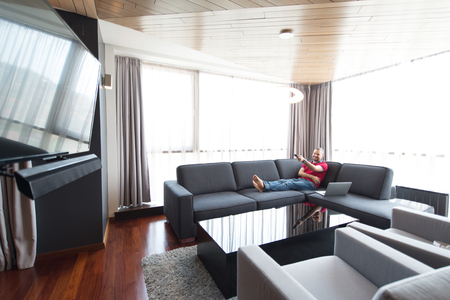 young handsome man enjoying free time watching television in his luxury home villaの写真素材