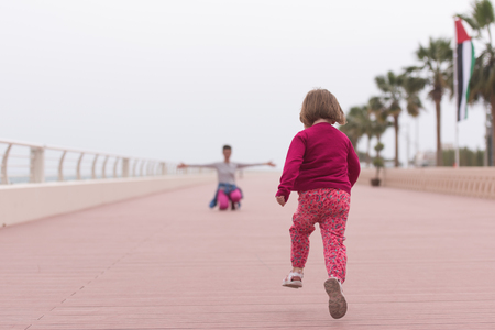 young mother and cute little girl running and cheerfully spend their time on the promenade by the seaの写真素材