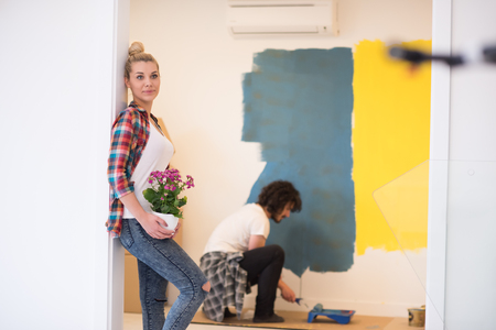Happy couple doing home renovations, the man is painting the room and the woman hold the pot with flowersの写真素材