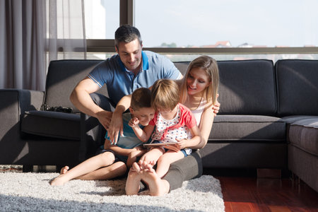 Happy Young Family Playing Together with tablet at home sitting on the sofaの写真素材