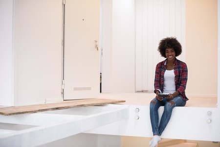 Attractive young african american woman sitting on stairs at home and smilingの写真素材