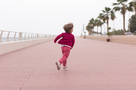 cute little girl running and cheerfully spend her time on the promenade by the seaの写真素材
