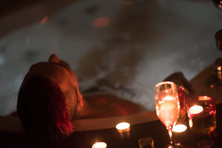 young handsome man enjoys relaxing in the hot tub with candles and champagne at luxury resort spaの写真素材