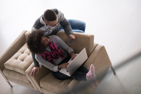 Happy young multiethnic couple shopping online through laptop using credit card at homeの写真素材