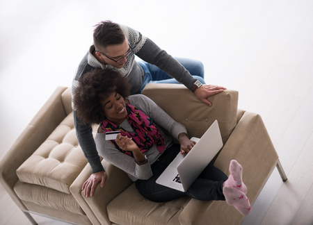 Happy young multiethnic couple shopping online through laptop using credit card at homeの写真素材