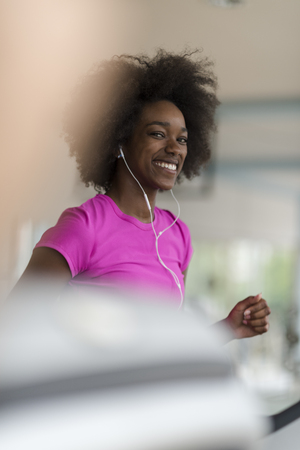 afro american woman running on a treadmill at the gym while listening music on earphonesの写真素材