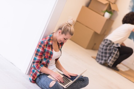 Happy couple doing home renovations, the man is painting the room and the woman is relaxing on the floor and connecting with a laptopの写真素材