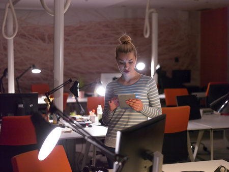young female entrepreneur working on digital tablet in night officeの写真素材
