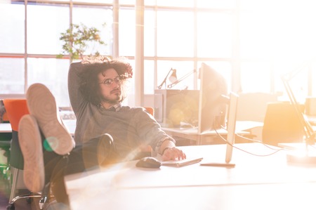 Full length of a relaxed casual young businessman sitting with legs on desk at officeの写真素材