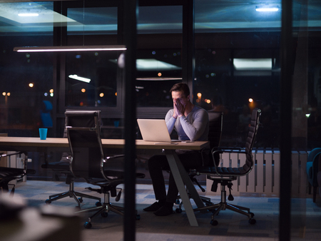 Young man working on laptop at night in dark office. The designer works in the later time.